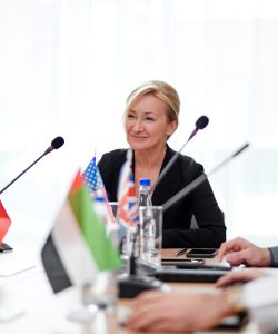 adult caucasian female delegate in formalwear looking at audience female delegate in formalwear looking at audience, giving speech report at multi-ethnic conference, meeting in boardroom, using microphones