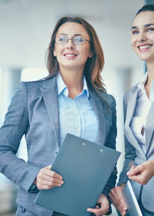 Image of two confident businesswomen in formalwear looking forwards